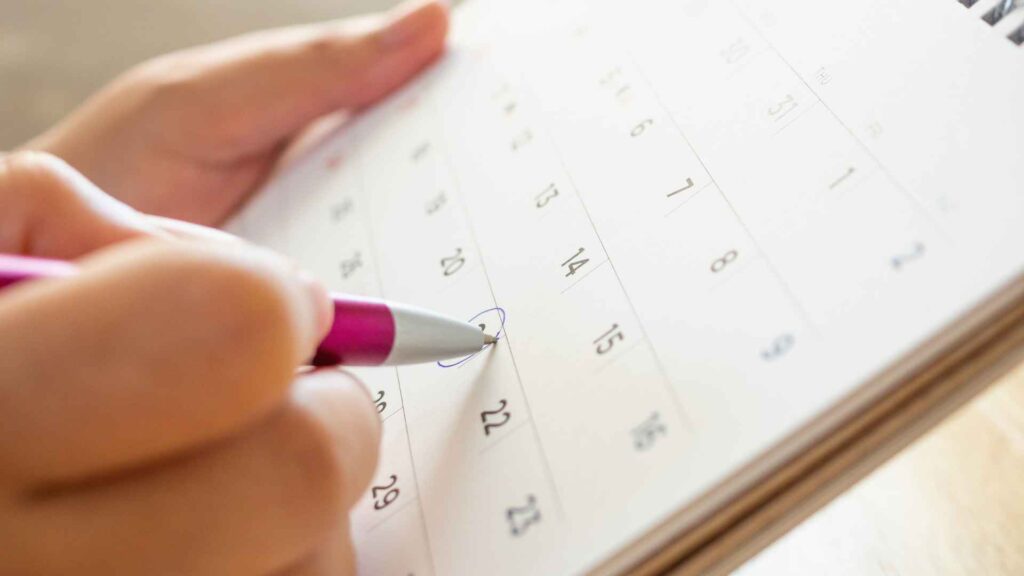 In diesem Bild ist ein Kalender zu sehen, in den gerade von Hand mit dem Kugelschreiber Vermerke eingetragen werden.