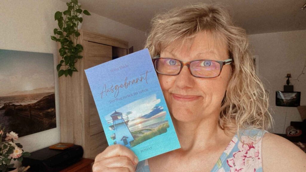 Die Autorin dieses Blogartikels, Britta Thiele, ist zu sehen. Sie hält ihren ersten eigenen Roman mit dem Titel "Ausgebrannt - der Weg zurück ins Leben" in der Hand.