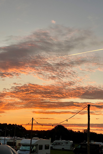 Ein traumhafter Sonnenaufgang über dem Campingplatz ist zu sehen. Der Himmel leuchtet in schönstem Orange und Gelb.