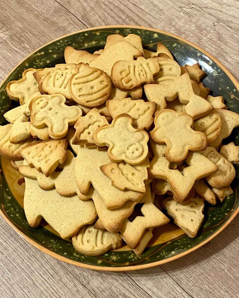 Die fertigen Plätzchen sind auf einem Weihnachtsteller angerichtet. Es sind ausgestochene Lebkuchenmänner, Christbaumkugeln, Tannenbäume und Sterne.