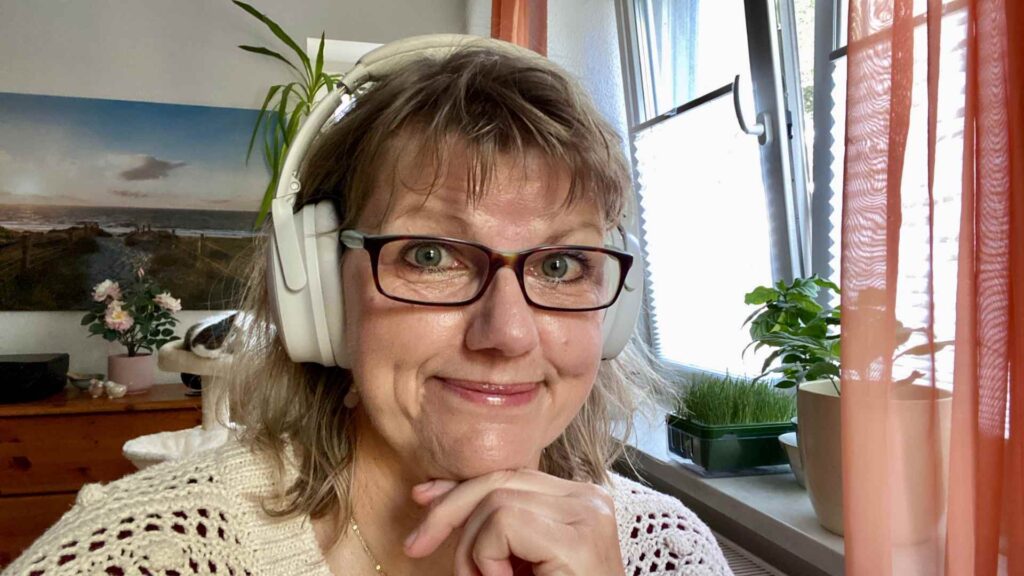 Ich sitze an meinem Schreibtisch und lächle in die Kamera. Auf dem Kopf habe ich meine Kopfhörer, die den Baulärm zuverlässig abhalten.